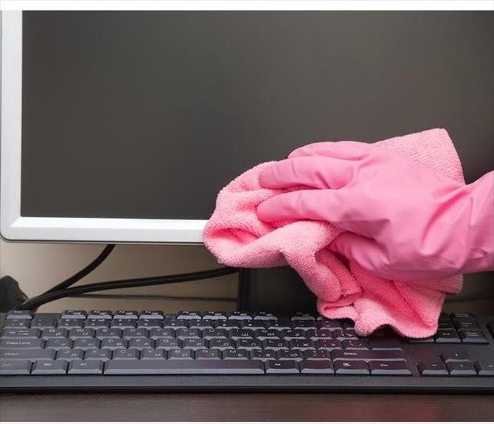hand with a pink glove wiping a computer monitor with a pink rag